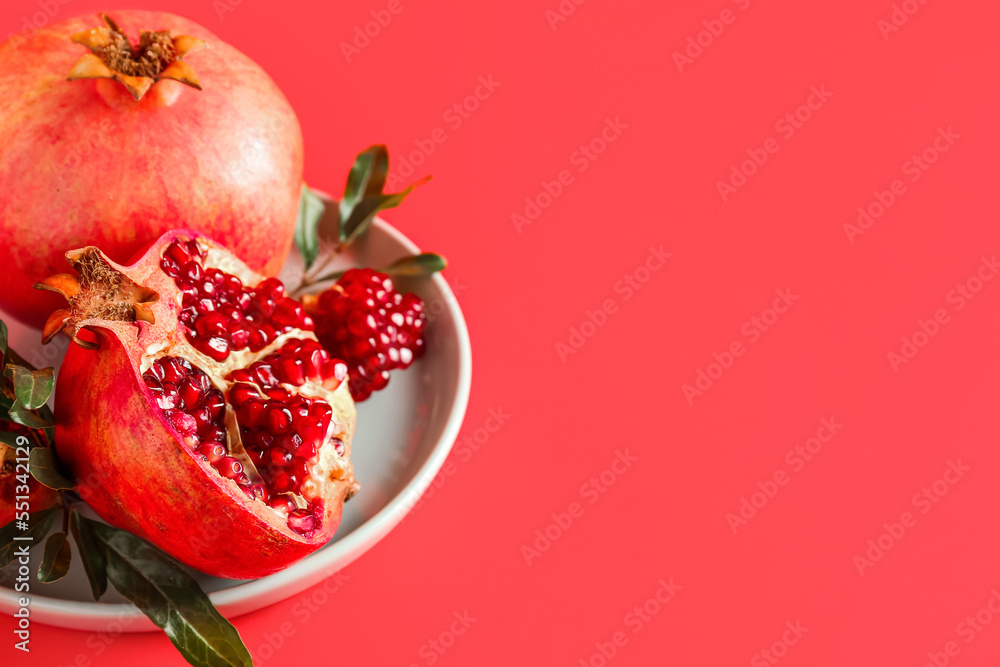 Plate with fresh pomegranates on red background