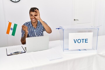 Canvas Print - Young handsome hispanic man at political campaign election holding india flag smiling happy doing ok sign with hand on eye looking through fingers