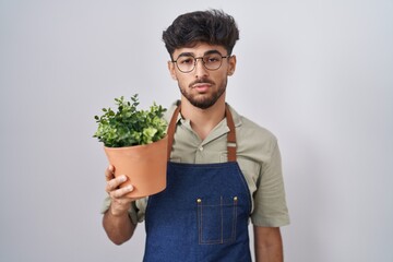 Sticker - Arab man with beard holding green plant pot looking sleepy and tired, exhausted for fatigue and hangover, lazy eyes in the morning.