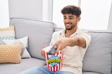 Sticker - Young arab man eating popcorn watching movie at home