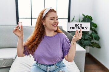 Wall Mural - Young redhead woman smiling confident holding menstrual cup and eco friendly banner at home