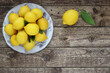 Fresh lemons fruit on plate on wooden table. Top view. Decorative arrangement of lemons with leaves on wood background.