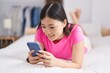 © Krakenimages.com - Chinese woman using smartphone lying on bed at bedroom