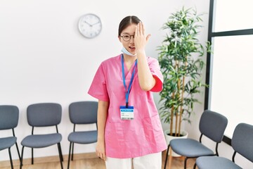 Wall Mural - Young asian nurse woman at medical waiting room covering one eye with hand, confident smile on face and surprise emotion.