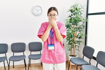 Wall Mural - Young asian nurse woman at medical waiting room shocked covering mouth with hands for mistake. secret concept.