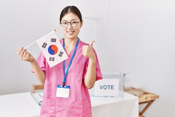 Sticker - Young asian nurse woman at political campaign election holding south korea flag smiling happy and positive, thumb up doing excellent and approval sign