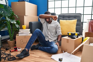 Sticker - African american man sitting on the floor at new home covering eyes with arm smiling cheerful and funny. blind concept.