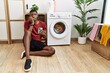 Young african american man using smartphone waiting for washing machine looking stressed and nervous with hands on mouth biting nails. anxiety problem.