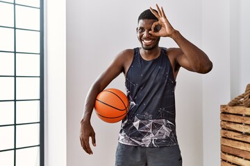 Sticker - Young african american man holding basketball ball at home smiling happy doing ok sign with hand on eye looking through fingers