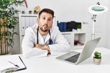 Poster - Young doctor working at the clinic using computer laptop making fish face with lips, crazy and comical gesture. funny expression.