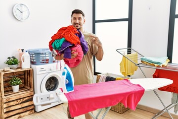 Canvas Print - Young handsome man holding laundry ready to iron smiling happy pointing with hand and finger