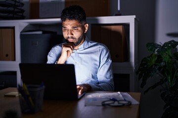 Poster - Hispanic man with beard working at the office with laptop at night serious face thinking about question with hand on chin, thoughtful about confusing idea