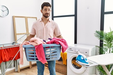 Sticker - Young man with beard holding laundry basket smiling looking to the side and staring away thinking.