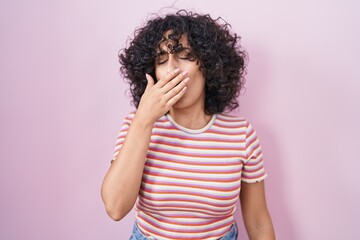 Poster - Young middle east woman standing over pink background bored yawning tired covering mouth with hand. restless and sleepiness.