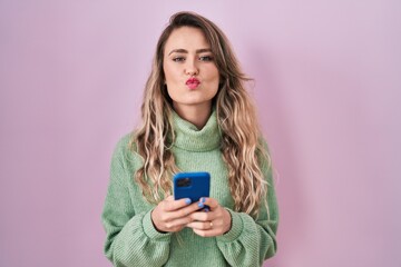 Canvas Print - Young caucasian woman using smartphone typing message looking at the camera blowing a kiss being lovely and sexy. love expression.