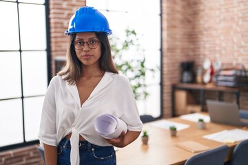 Poster - Hispanic young woman wearing architect hardhat at office thinking attitude and sober expression looking self confident