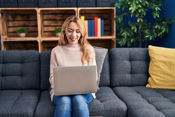 Wall Mural - Young woman using laptop sitting on sofa at home