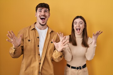 Poster - Young hispanic couple standing over yellow background celebrating mad and crazy for success with arms raised and closed eyes screaming excited. winner concept