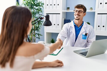 Canvas Print - Man and woman wearing doctor uniform having medical consultation handshaking at clinic