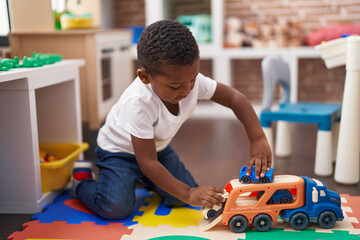 African american boy playing with cars and truck toy sitting on floor at kindergarten