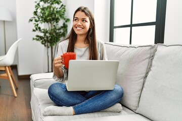 Sticker - Young latin woman using laptop and drinking coffee sitting on sofa at home