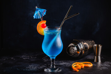 Wall Mural - Glass of blue lagoon cocktail decorated with orange and cherry at festive bar counter background.