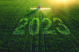 Fototapeta Kawa jest smaczna - 2023 Happy New Year agricultural business concept. Aerial view of farming tractor plowing and spraying on green field.
