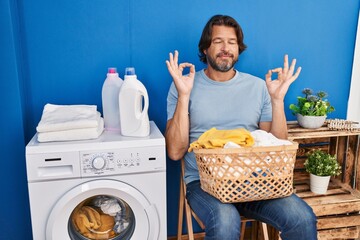 Wall Mural - Handsome middle age man waiting for laundry relax and smiling with eyes closed doing meditation gesture with fingers. yoga concept.