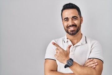 Canvas Print - Young hispanic man with beard wearing casual clothes over white background with a big smile on face, pointing with hand finger to the side looking at the camera.