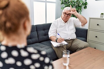 Sticker - Senior psychologist man at consultation office making fun of people with fingers on forehead doing loser gesture mocking and insulting.