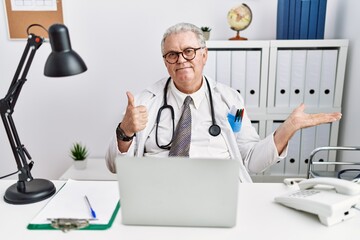 Canvas Print - Senior caucasian man wearing doctor uniform and stethoscope at the clinic showing palm hand and doing ok gesture with thumbs up, smiling happy and cheerful