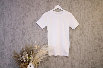 Canvas Print - White shirt blank mockup on a hanger on the grey background with dry grass

