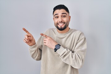 Canvas Print - Young handsome man standing over isolated background pointing aside worried and nervous with both hands, concerned and surprised expression