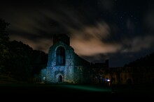 Night Shot Of Ruins Of Famous Fountains Abbey Monastery In England Against A Cloudy Dark Starry Sky.