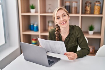 Wall Mural - Young blonde woman using laptop reading document at home