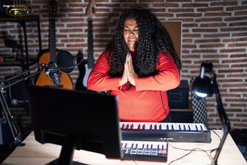 Wall Mural - Plus size hispanic woman playing piano at music studio begging and praying with hands together with hope expression on face very emotional and worried. begging.