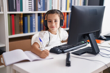 Canvas Print - Adorable hispanic girl student using computer and headphones writing on notebook at classroom