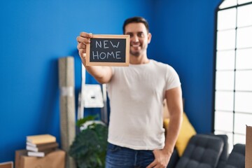 Canvas Print - Young hispanic man smiling confident holding blackboard with message at new home