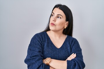 Sticker - Young brunette woman standing over isolated background looking to the side with arms crossed convinced and confident