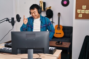 Poster - Young chinese man looking at online music tutorial smiling happy pointing with hand and finger to the side