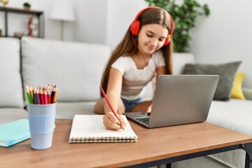 Wall Mural - Adorable girl doing homework using laptop at home