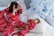 © Olena - People in same family look red pajamas, kidding at home christmas day. Happy funny kid child son with mother spend time together, enjoying, fool around in bed in bedroom. New Year holidays. Homeliness