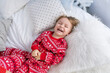 © Olena - Smiling toddler boy in Christmas red pajamas is playing while lying on bed. Child fun, enjoying, fool around, kidding in bedroom at home. Celebrating New Year holidays. Childhood concept. Copy space
