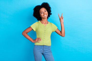 Photo of optimistic nice positive girl with perming coiffure green t-shirt showing v-sign hand on waist isolated on blue color background