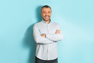 Poster - Male portrait. Happy middle aged caucasian man with folded arms smiling at camera, posing over blue studio background