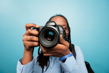 Wall Mural - Amateur photographer taking photos with modern DSLR device while standing on blue background. Photography entusiast enjoying taking pictures with photo camera. Studio shot