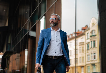 A handsome mature business man is walking through the city street near the office building.