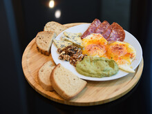 Closeup Shot Of A Breakfast Dish With Eggs, Salami, And Guacamole On A Wooden Board With Bread