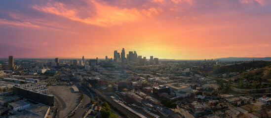 panoramic aerial shot of the skyscrapers and office buildings in the city skyline over Los Angeles State Historic Park with lush green trees with powerful clouds at sunset in Los Angeles California