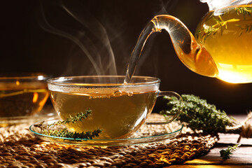 Wall Mural - Pouring aromatic herbal tea into cup and thyme on wooden table